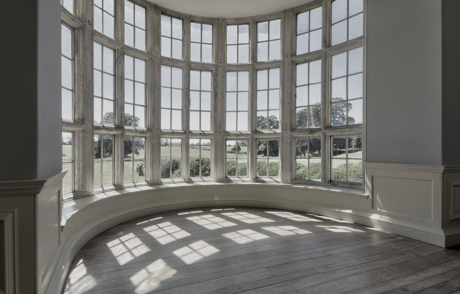 A curved bay window casting sunlight patterns on a wood floor