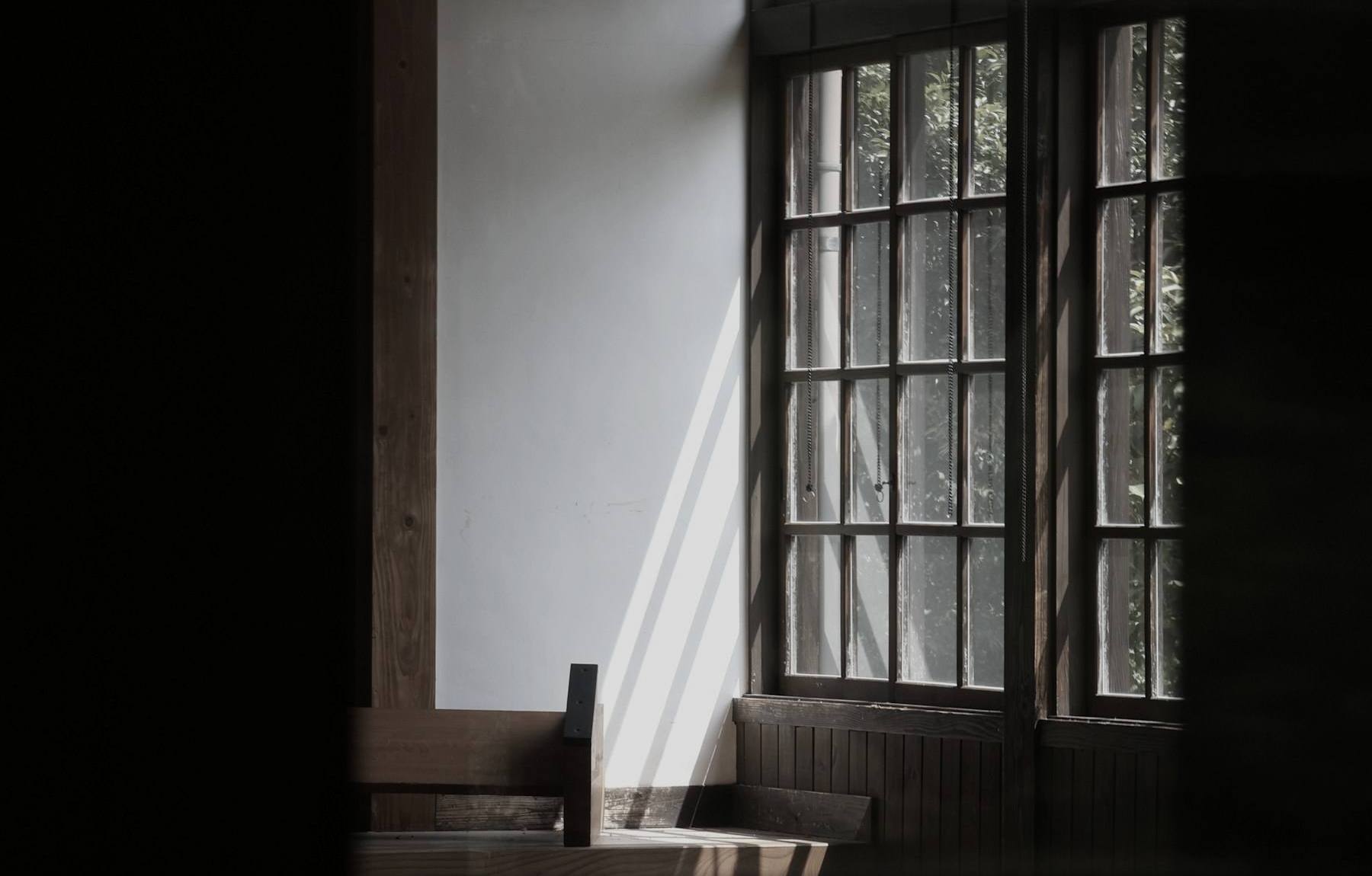 Daylight through a wood framed window onto a white wall in a dark room
